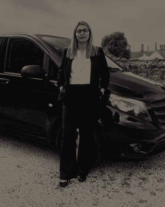 Alexandra, owner of Funerals LTD, standing beside the company's funeral transport vehicle.